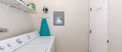 A laundry room with a washing machine, a drying rack, and a shelf with laundry supplies.