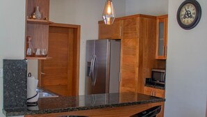 A modern kitchen with wooden cabinets, a stainless steel refrigerator, two bar stools, and a pendant light. - Puerto Plata House Full of Peace ❤️ (puerto plata)