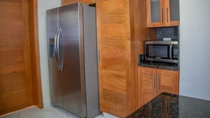 A kitchen with wooden cabinets, a stainless steel refrigerator, and a microwave on the countertop. - Puerto Plata House Full of Peace ❤️ (puerto plata)