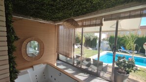 Ein modernes Badezimmer mit einer großen Badewanne, einem runden Spiegel und Blick auf einen Pool.
