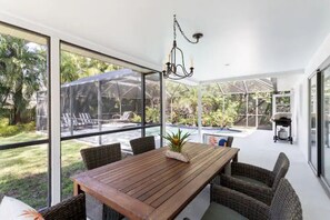 Enjoy meals at the large dining table surrounded by wicker chairs, with expansive views of the lush garden and pool area.