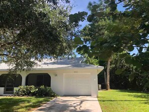 Stylish single-story home with a garage, surrounded by lush greenery and mature trees.