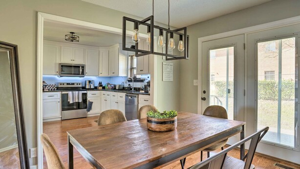 A modern kitchen with white cabinets, a wooden dining table, and a hanging light fixture.