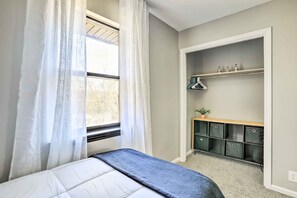 Une chambre avec un lit, une fenêtre avec des rideaux légers, une étagère intégrée avec des tiroirs de rangement et une petite plante.