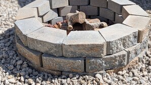 A circular stone fire pit with a log in the center, surrounded by gravel.