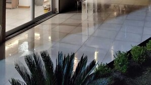 A modern building with large glass doors and windows, a tiled patio area, and outdoor seating.
