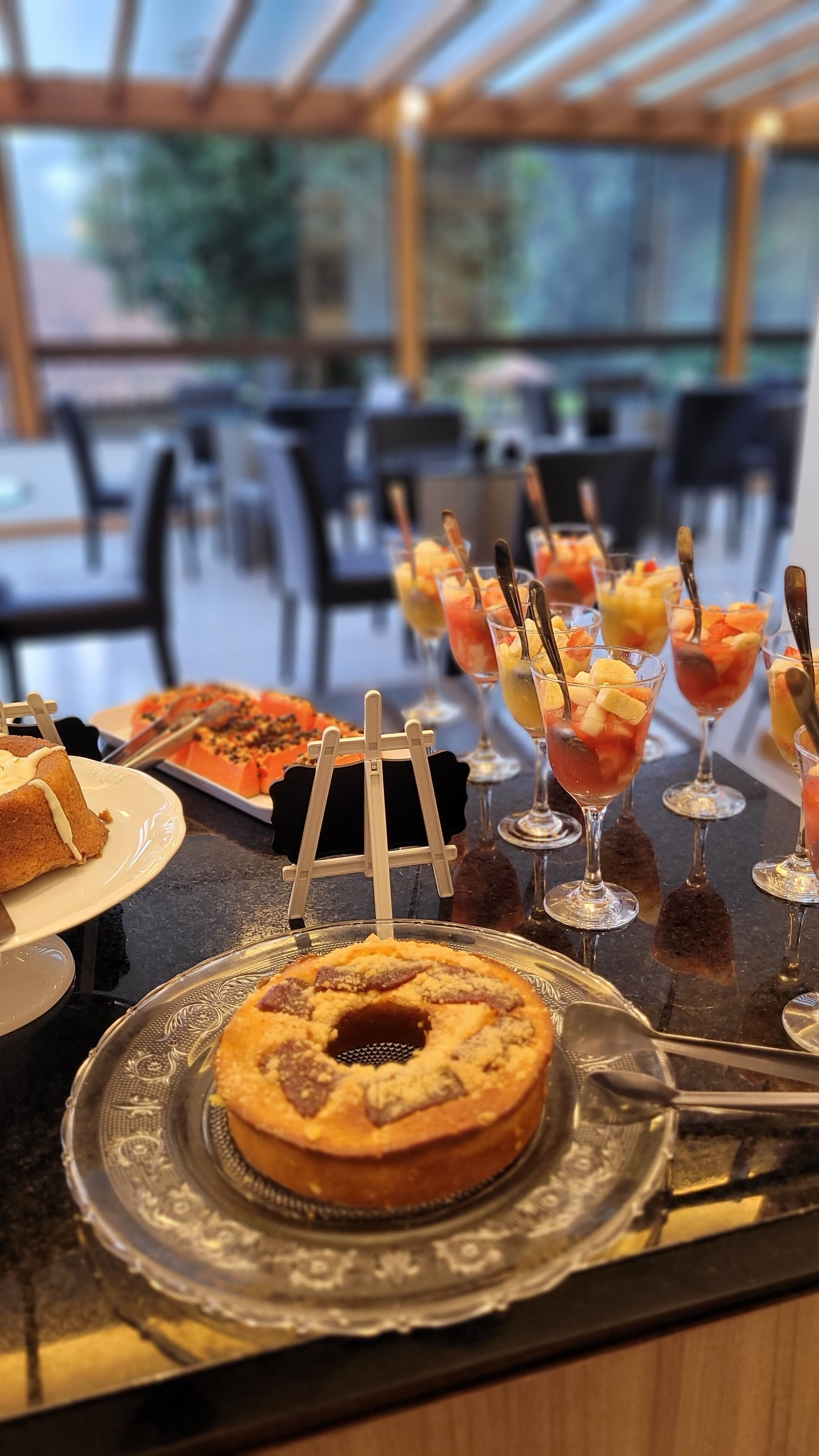 A buffet table with various desserts and drinks, including a bundt cake and fruit parfaits.