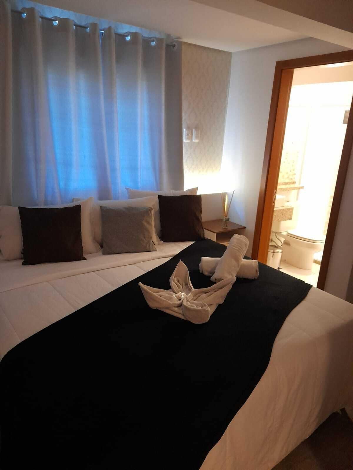 A hotel room with a bed, a nightstand, and a window with curtains.