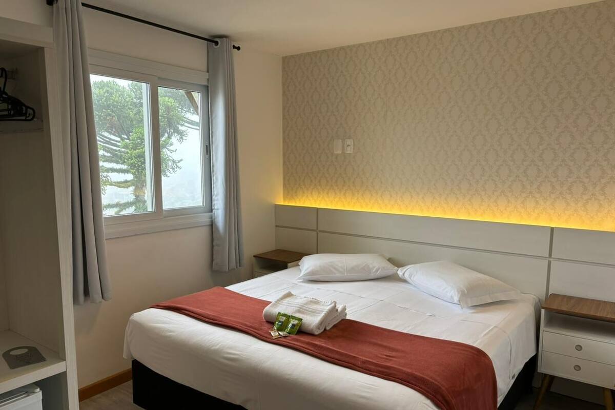 A hotel room with a bed, a nightstand, a wardrobe, and a window with curtains.