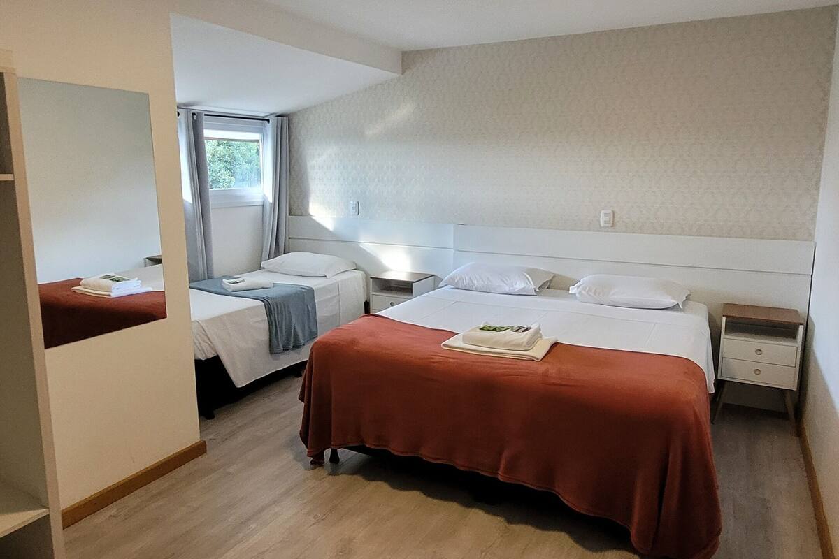 A hotel room with two beds, a wooden floor, a window with curtains, and a ceiling light.