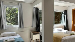A hotel room with two beds, a small bedside table, and a window with curtains.