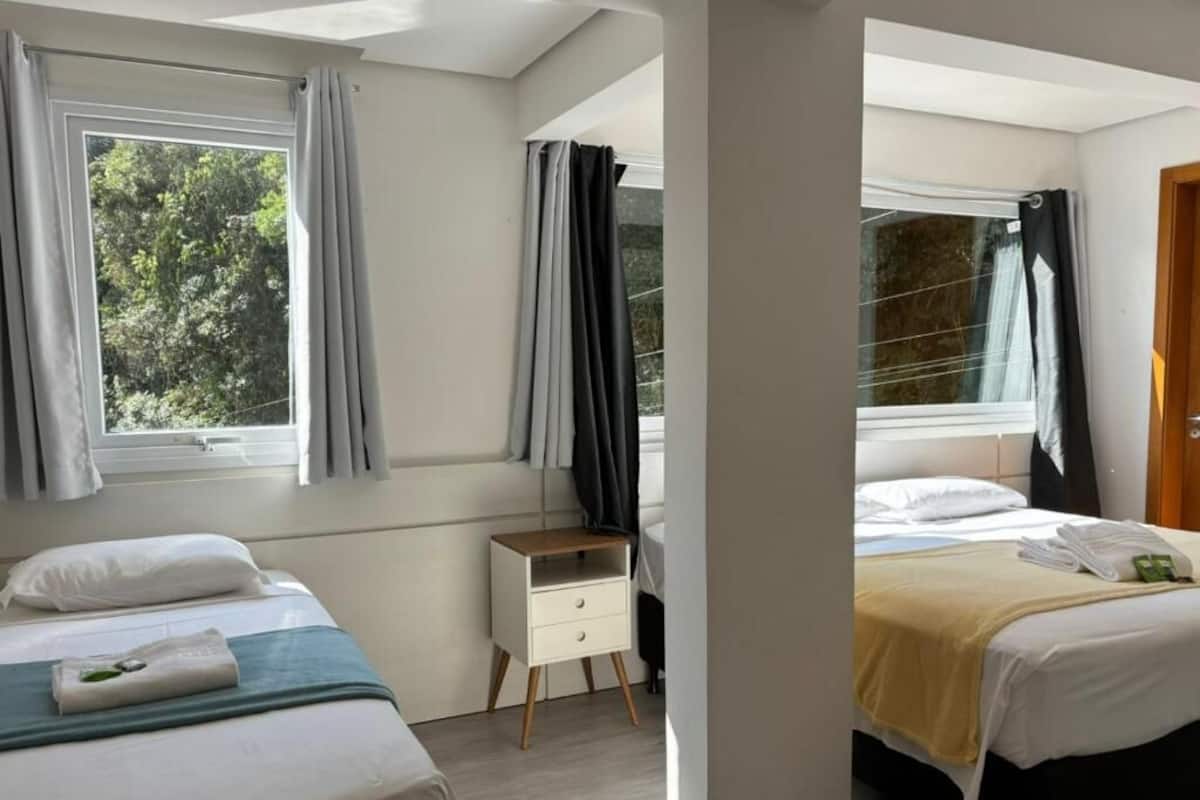 A hotel room with two beds, a small bedside table, and a window with curtains.