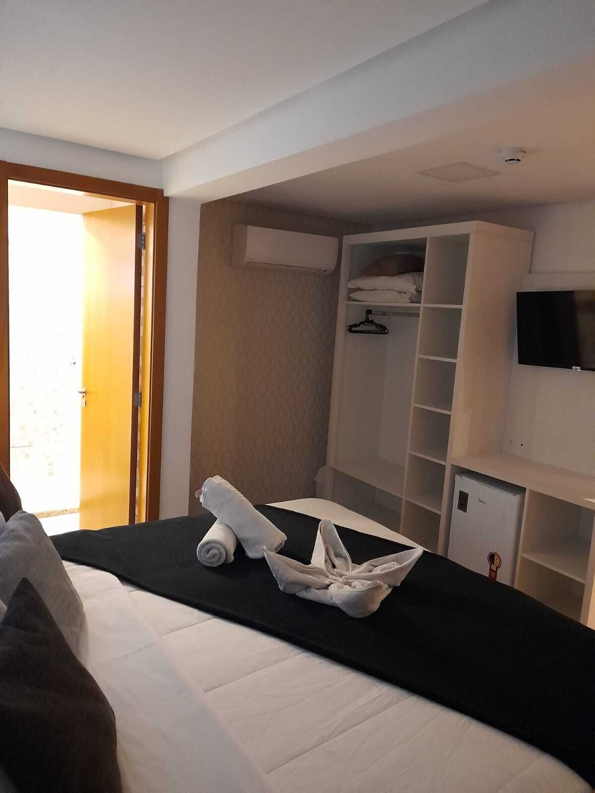 A hotel room with a bed, a wardrobe, a TV, and a door leading to the outside.