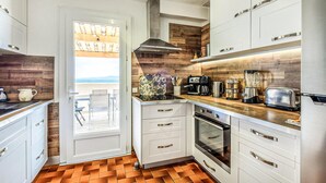 Une cuisine moderne avec des armoires blanches, un pare-feu en bois et une vue sur un balcon extérieur, accessible par une porte ouverte.