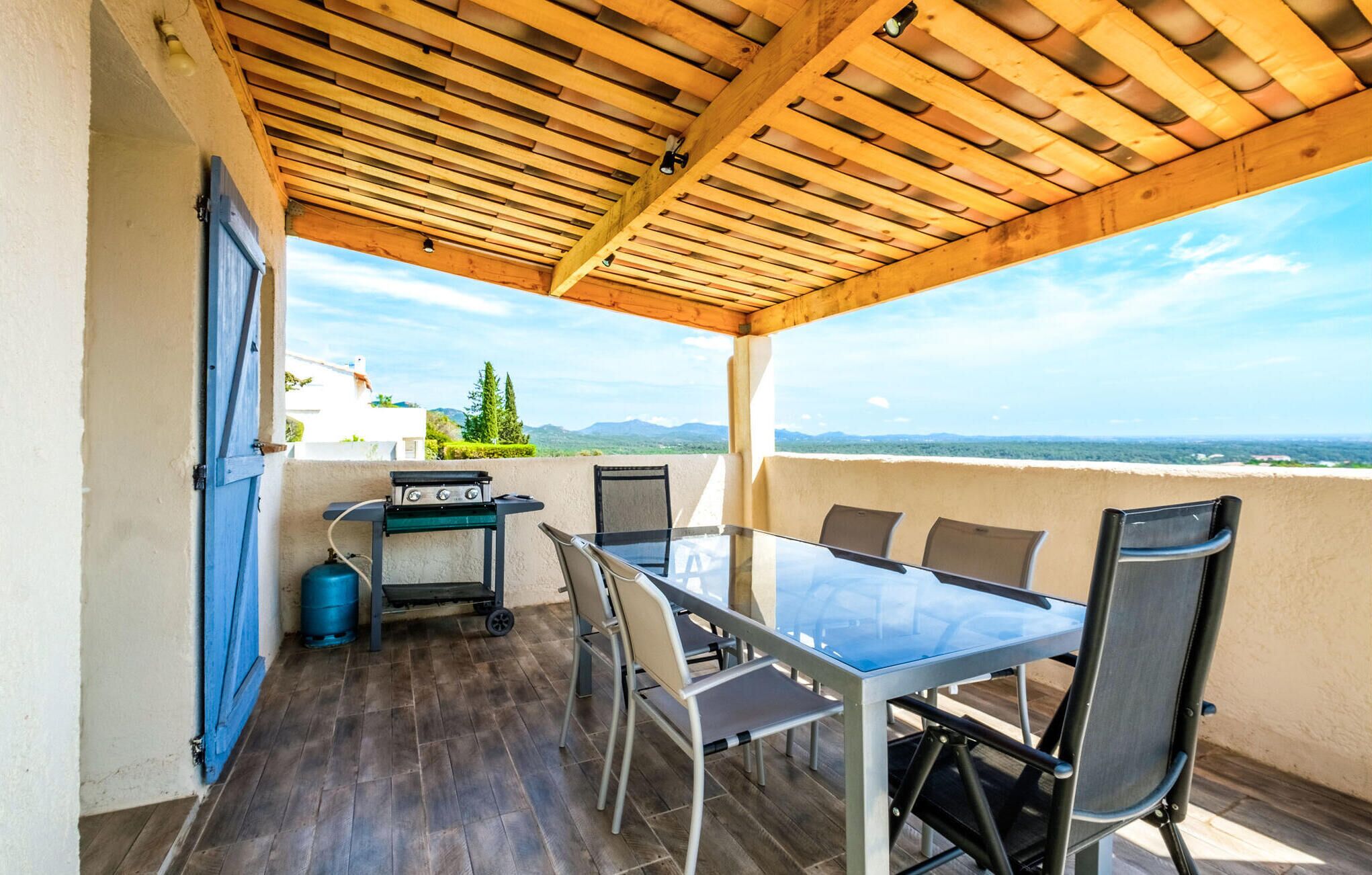 Un patio techado al aire libre con mesa y sillas, una parrilla y vistas del paisaje.