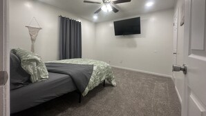 A bedroom with a bed, a ceiling fan, a TV, and a door. - The Simple Dwelling Place (Sulphur)