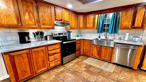 A kitchen with wooden cabinets, a stainless steel dishwasher, and a tiled backsplash. - The Simple Dwelling Place (Sulphur)