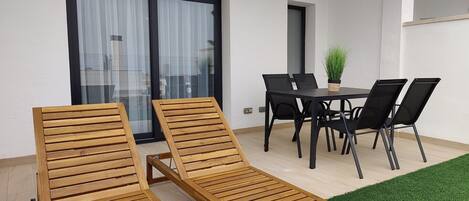 A patio with two wooden lounge chairs, a table, and four chairs.