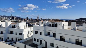 Un quartier urbain moderne, avec des bâtiments blancs, un ciel bleu dégagé et une vue lointaine sur les gratte-ciel de la ville.