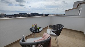 Un balcon avec deux fauteuils en osier, une petite table ronde sur laquelle se trouvent une bouteille, un verre et un pot de fleurs.
