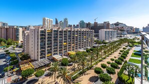 Een hoog appartementencomplex met meerdere balkons, omringd door palmbomen en een strand op de achtergrond.