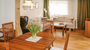 Un coin repas avec une table en bois, des chaises et un vase de fleurs. On aperçoit un canapé et une lampe au fond.