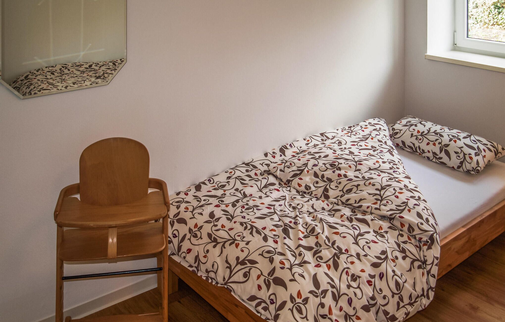 Une petite chambre simple, avec un lit simple, une chaise en bois et une fenêtre.