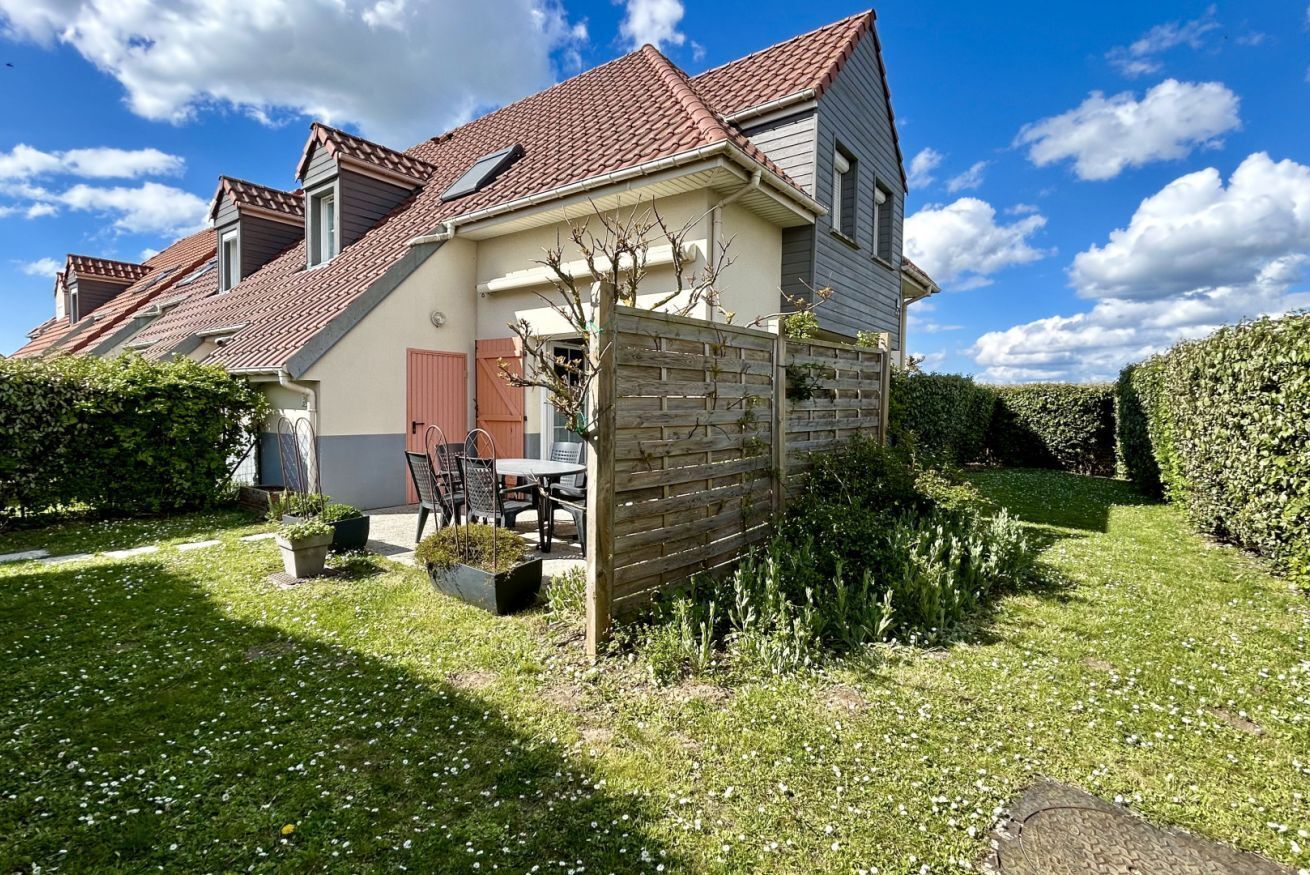 Een huis met twee verdiepingen, een dak met rode tegels, een houten omheining en een verzorgde tuin.