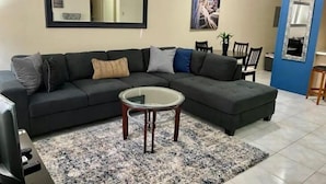 A living room with a sectional sofa, a glass coffee table, and a blue accent wall.