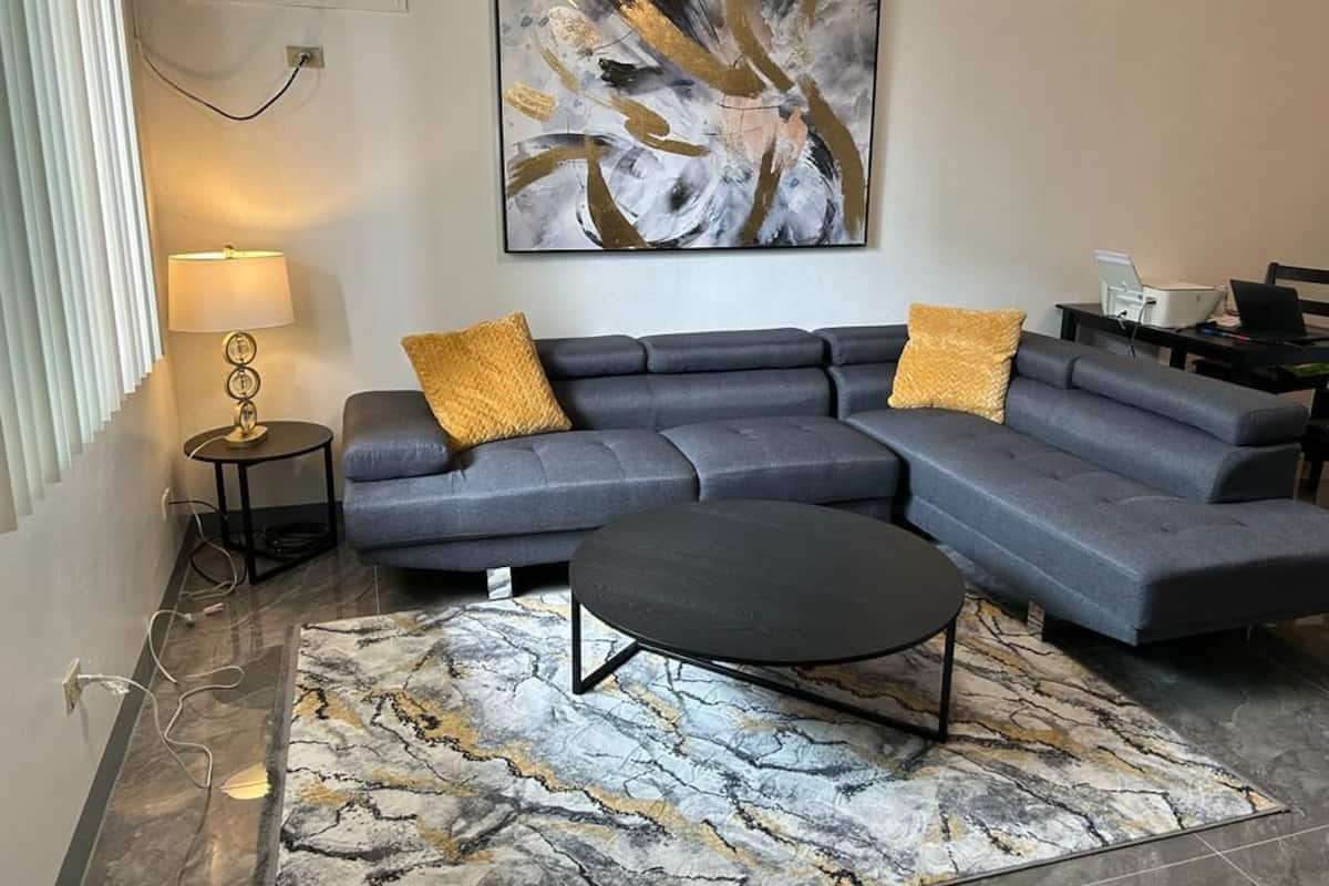 Ein modernes Wohnzimmer mit einer Eckcouch, einem runden Couchtisch und einem gemusterten Teppich.