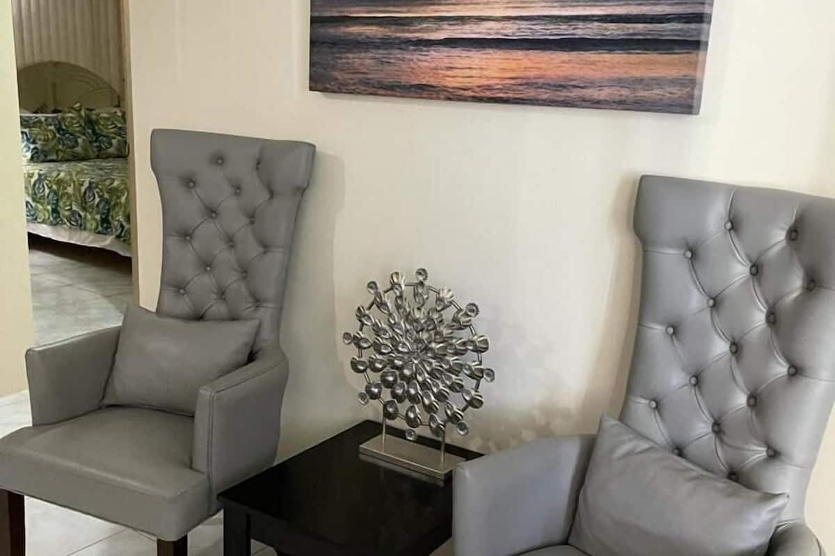 Zwei graue Ohrensessel stehen sich gegenüber, dazwischen ein kleiner Tisch. Auf dem Tisch steht eine Metallskulptur, an der Wand hängt ein Sonnenuntergangsbild.
