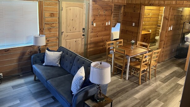 A cozy cabin interior with a sofa, dining table, and chairs.