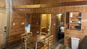 A wooden cabin interior with a dining area, a bathroom, and a small shelf with toiletries.