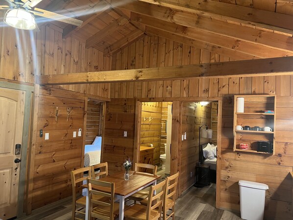 Interior de una cabaña de madera con comedor, baño y un pequeño estante con artículos de tocador.