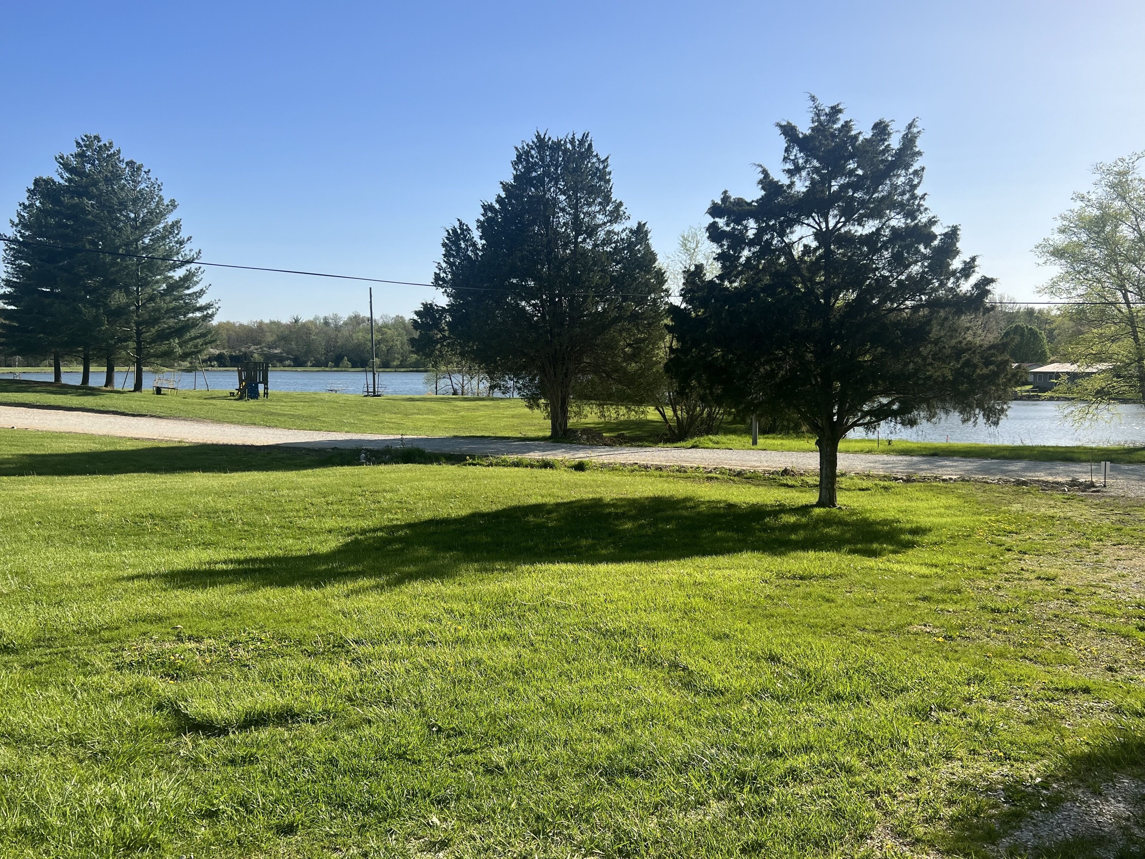 Un parque con césped, árboles, un lago y un sendero.