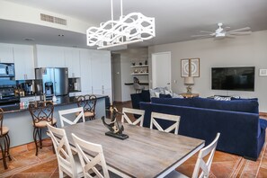 A modern kitchen with white cabinets, a built-in oven, and a dining area with a wooden table and white chairs.