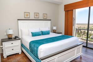 A hotel room with a large bed, a nightstand, a lamp, and a view of the landscape through a large window.