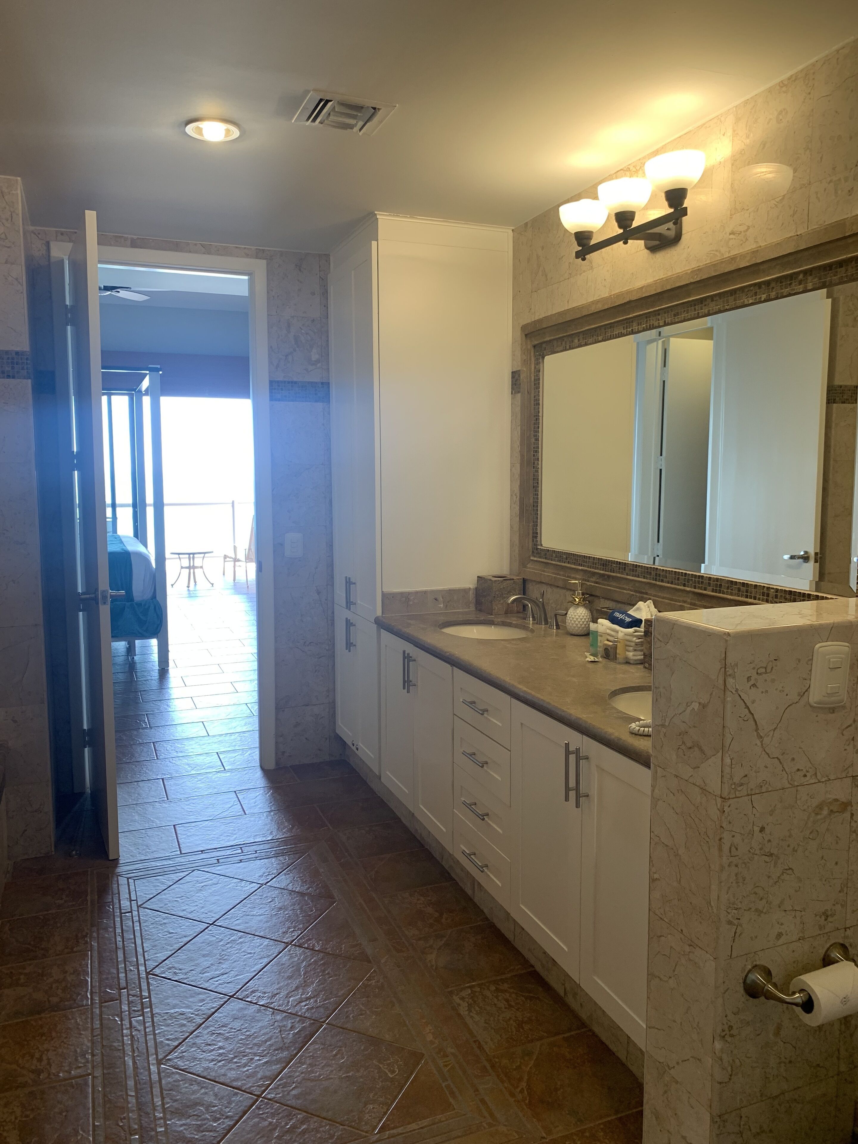Baño con espejo grande, lavamanos y retrete. Hay una puerta que da a un balcón.