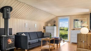 Un salon chaleureux avec un poêle à bois, un canapé, une petite table et une vue sur l’extérieur grâce à une porte vitrée.