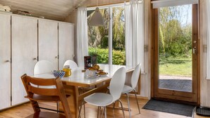 Un espace repas avec une table en bois, des chaises blanches et une vue sur la verdure environnante.