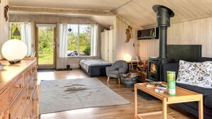 A cozy cabin interior with a wooden interior, a fireplace, a sofa, a desk, and a large window.