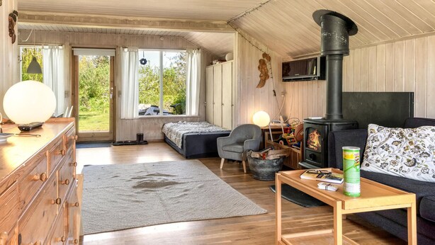 L’intérieur d’un chalet accueillant, avec un revêtement mural en bois, une cheminée, un canapé, un bureau et une grande fenêtre.