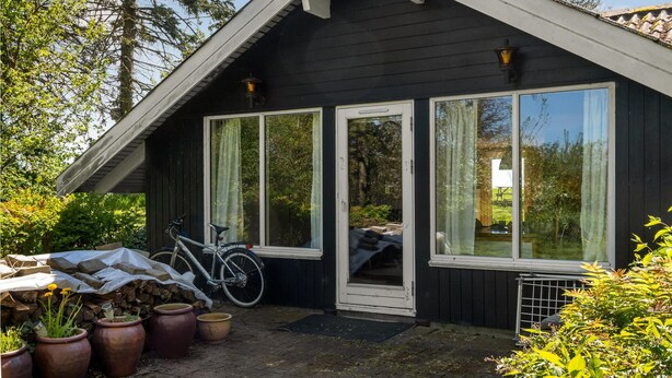 A small black cabin with a porch, large windows, and a bicycle parked outside.