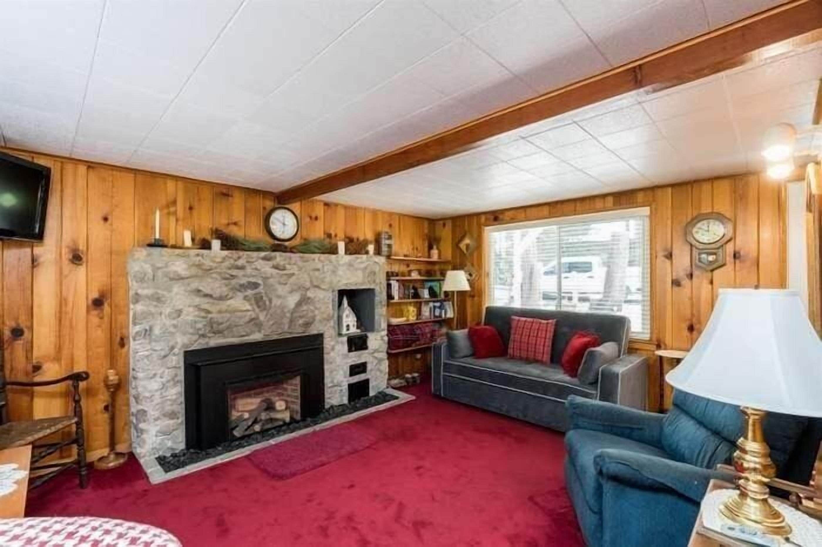 Un salon chaleureux avec une cheminée en pierre, des murs en bois, une moquette rouge et un canapé bleu.