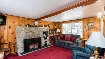 Un salon chaleureux avec une cheminée en pierre, des murs en bois, une moquette rouge et un canapé bleu.
