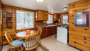 Una habitación estilo cabaña con paredes de madera, una mesa de comedor redonda y una zona de cocina con refrigerador y fregadero.