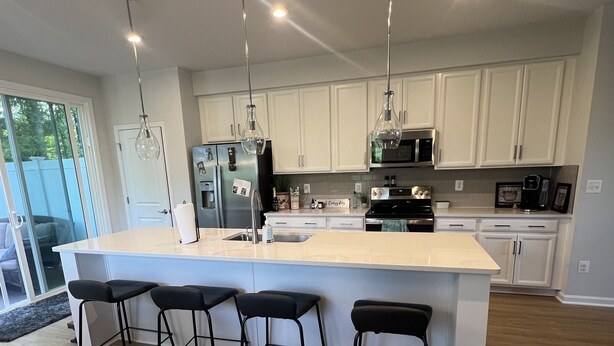 A modern kitchen with a large island, bar stools, stainless steel appliances, and pendant lighting.