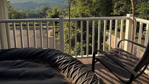 A balcony with a view of a parking lot and hills, a lamp post, and a chair.
