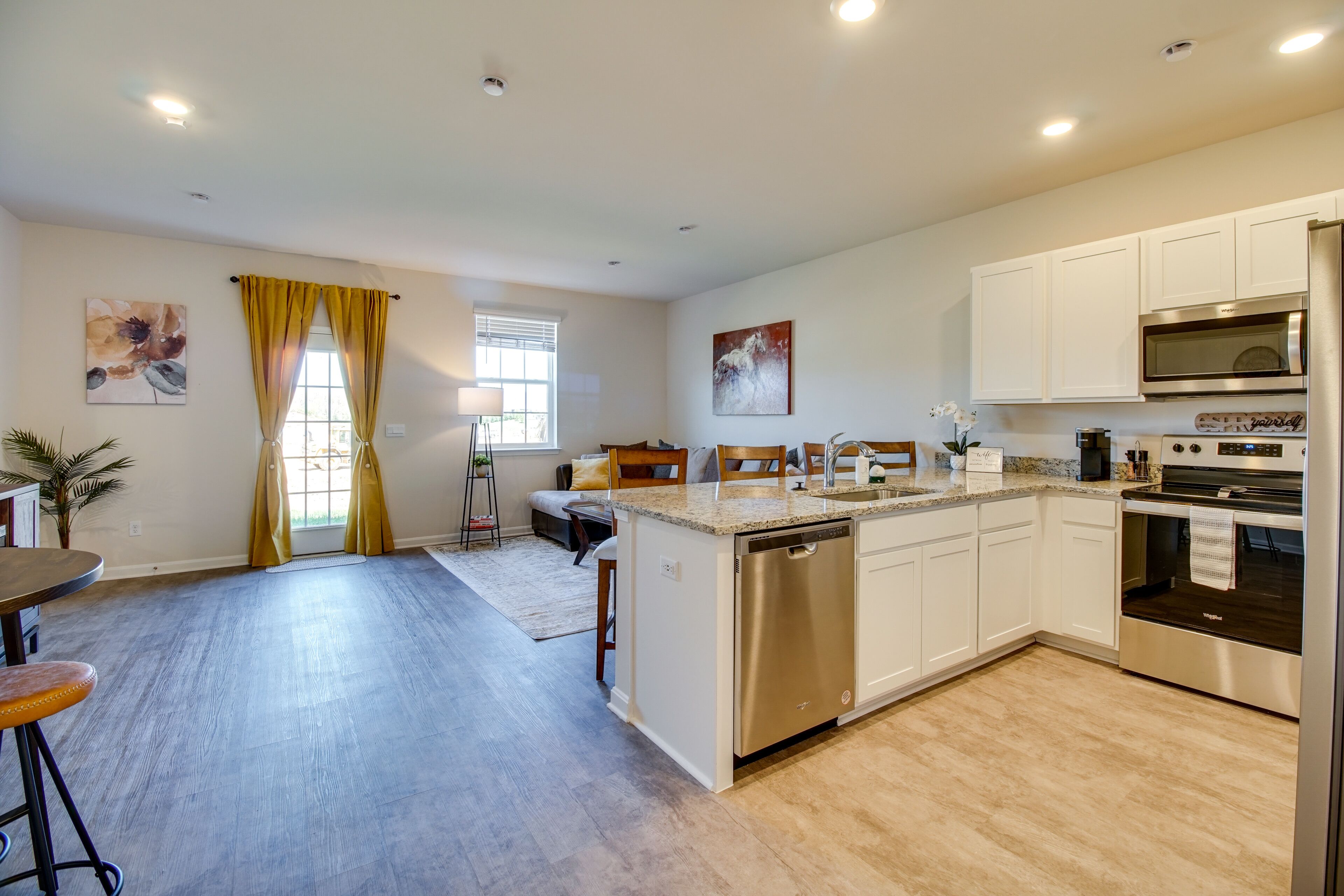 A modern kitchen with white cabinets, stainless steel appliances, and a wooden dining area.