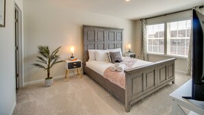 Een slaapkamer met een bed, nachtkastjes, een televisie en een raam met jaloezieën.